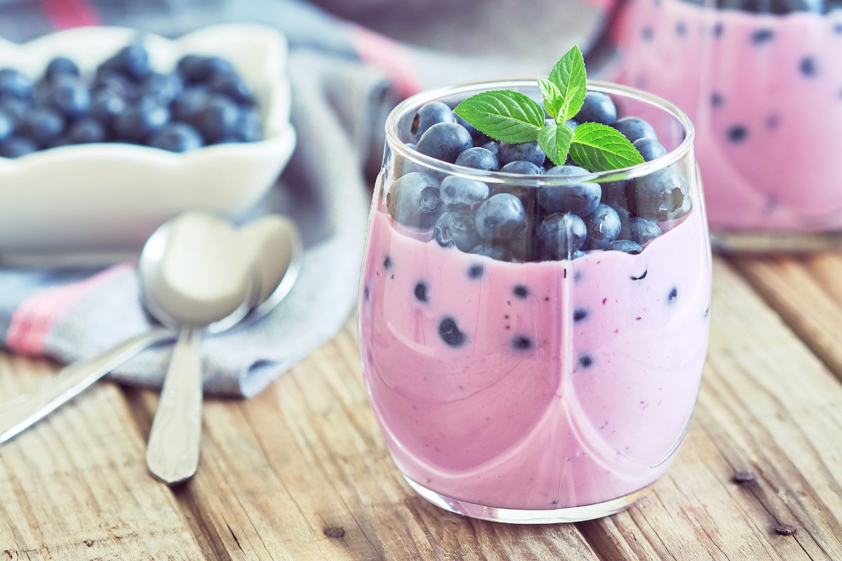 A glass of blueberry yogurt smoothie decorated with fresh blueberries and mint.