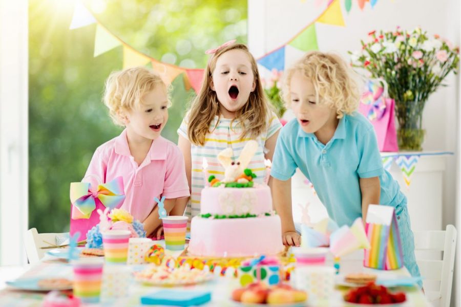 Kids blow candles on pink bunny decorated birthday cake.