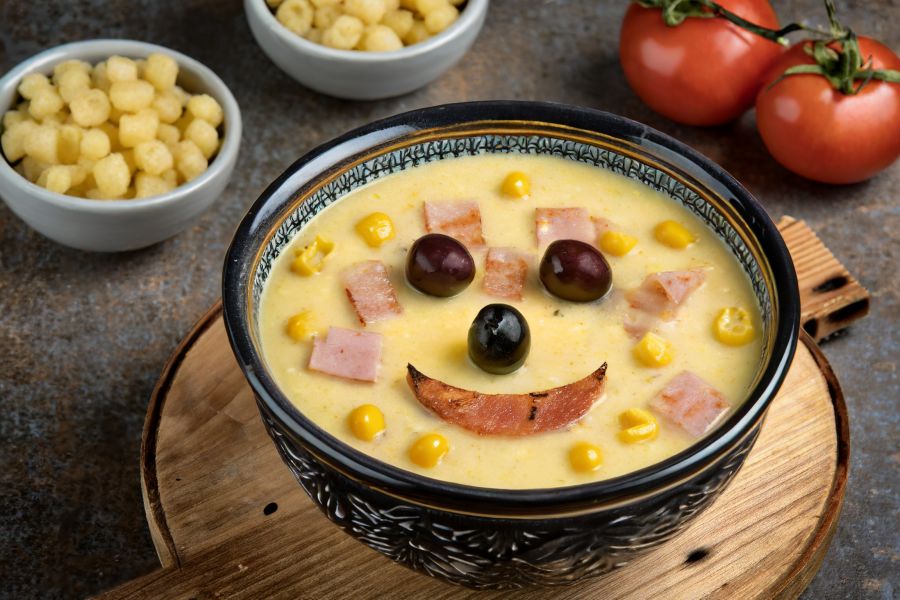 A bowl of ham and corn chowder with a silly face drawn on top.
