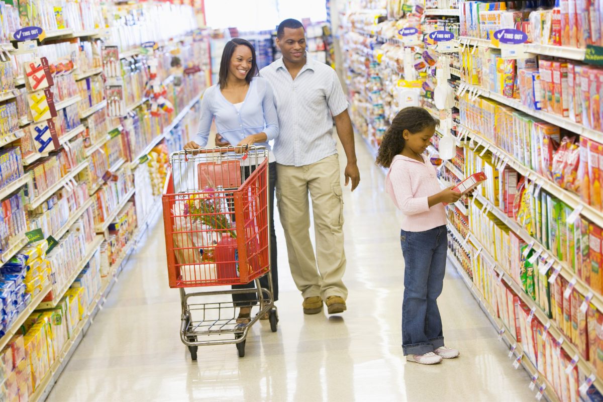 A girl checks a box of breakfast cereal while her parents watch her.