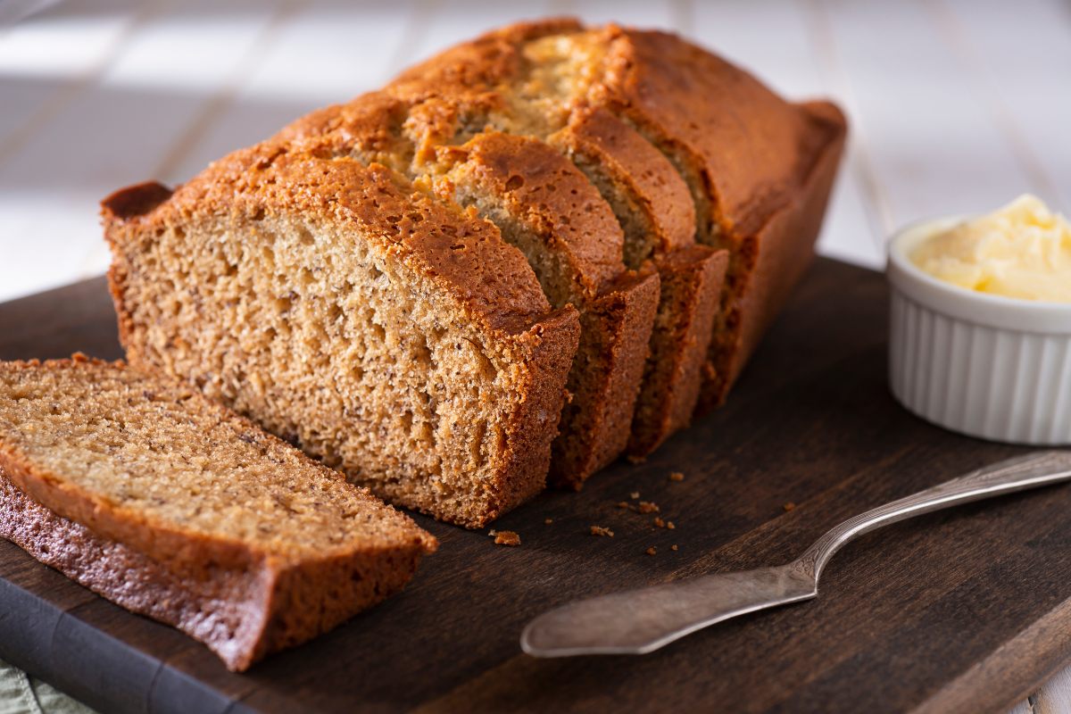 A loaf of applesauce and banana bread on a wooden board with butter on the side.