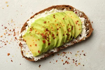 Toast with cream cheese, sliced avocado, and red chili flakes sprinkled on top.