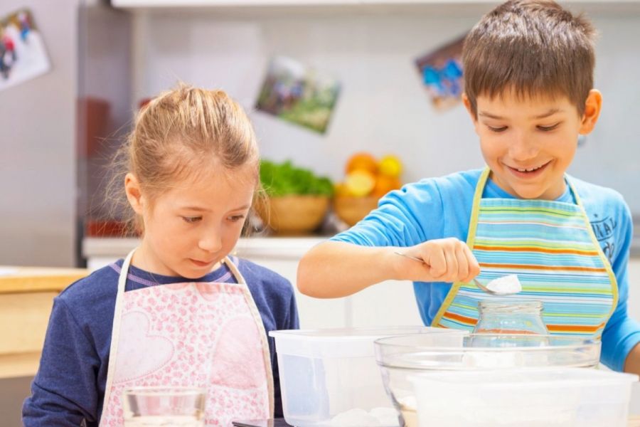 A boy measuring flour and a girl watching him.