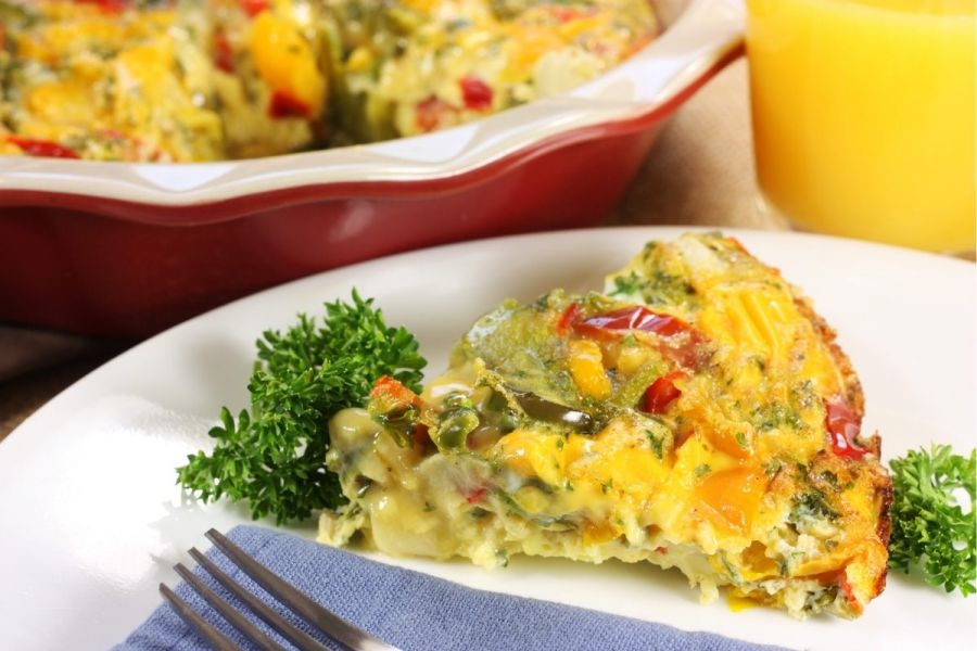 A piece of frittata made with sweet peppers on a plate, decorated with curly parsley.