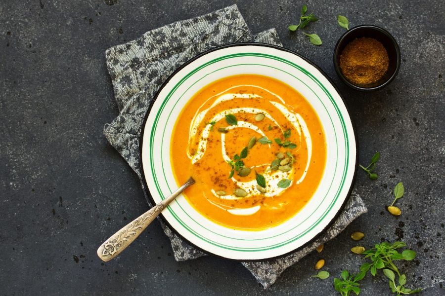 A soup plate wiht curried pumpkin soup garnished with yogurt and pumpkin seeds.