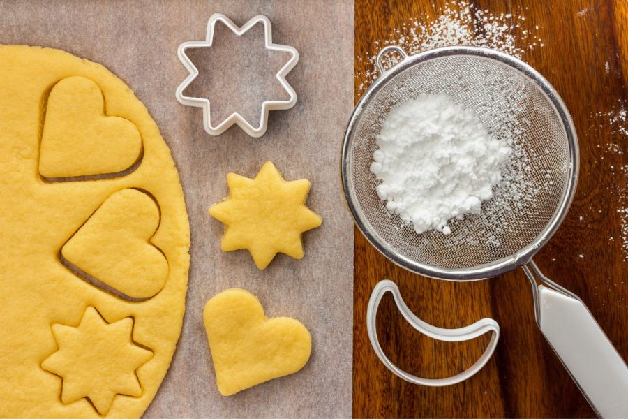 Cookie dough with shapes marked, cookie cutters and powdered sugar.