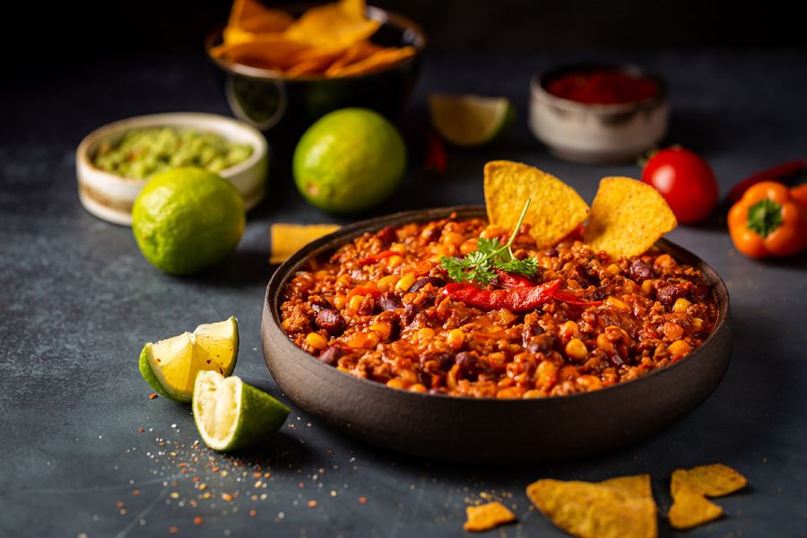 Mexican dip in a bowl with tortilla chips and mashed avocado on dark background.