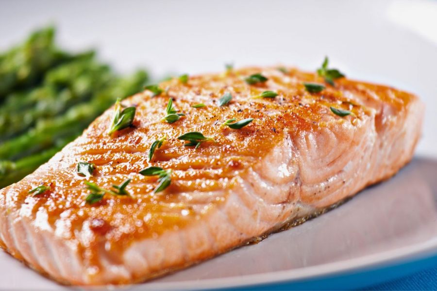 A plate with a fillet of salmon, cooked and garnished with herbs.
