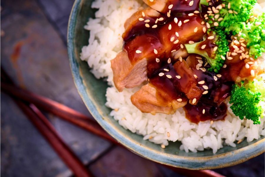 Chicken teriyaki served with rice and steamed broccoli, decorated with teriyaki sauce and sesame seeds.