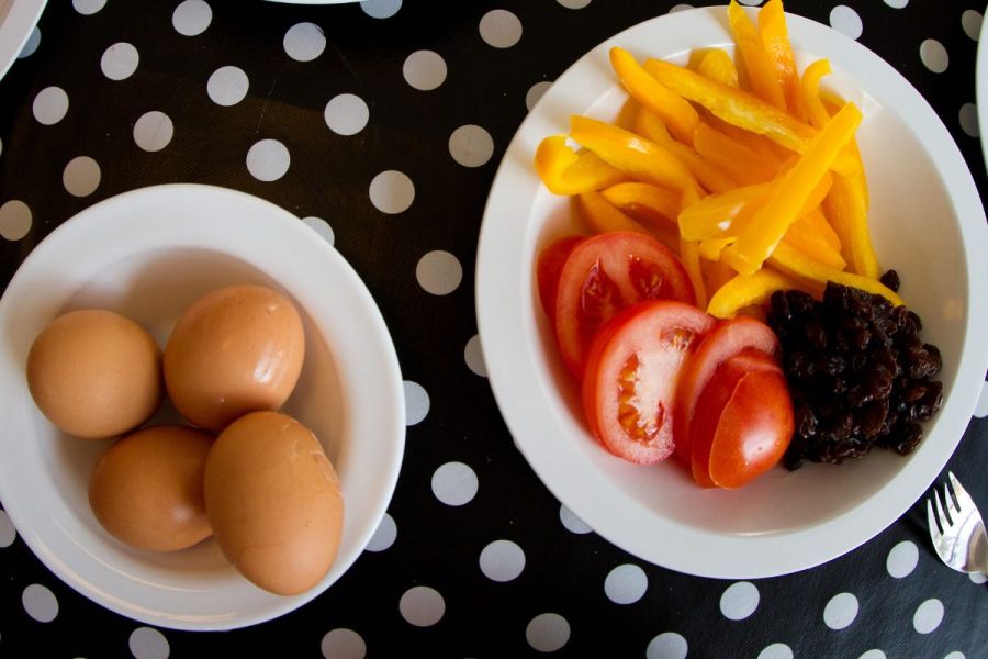 A kindergarden lunch with hard boiled eggs, chopped tomato, yellow pepper strips and raisins.