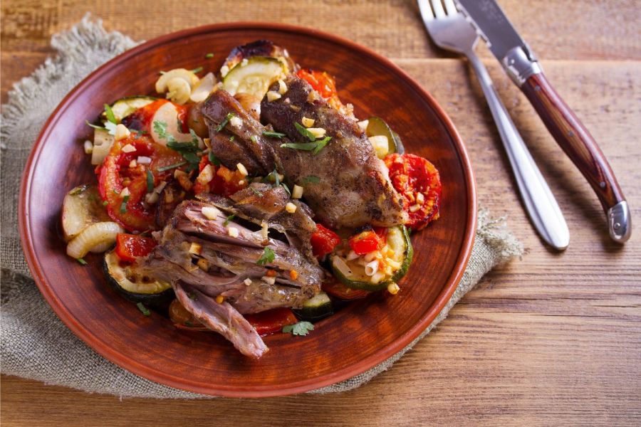 A plate with slow cooked lamb with vegetables and garlic.