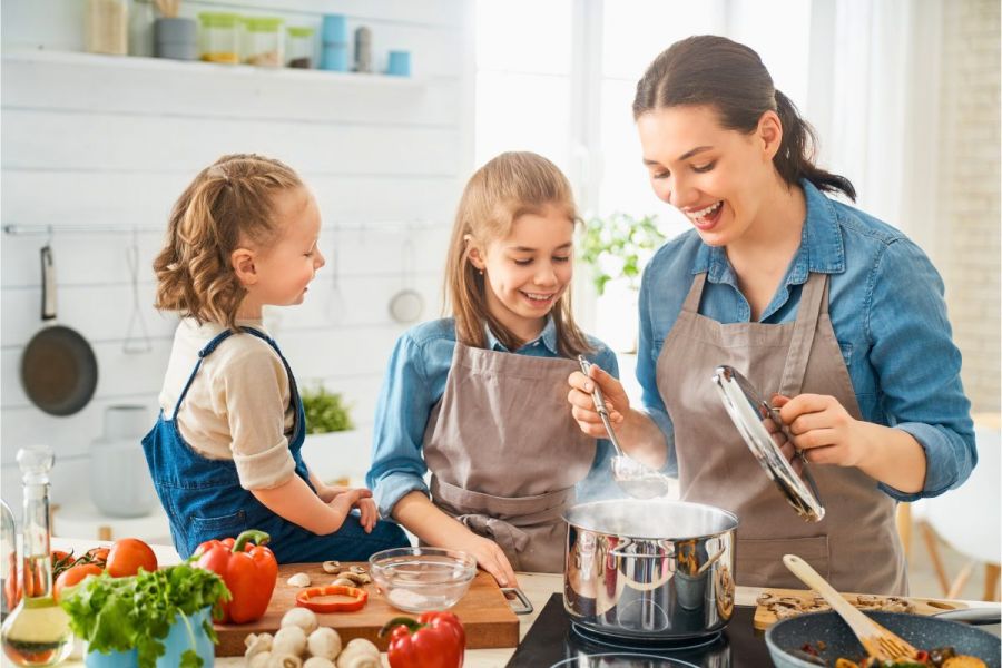 Mom cooking with girls in the kitchen, boiling food in a large pot.