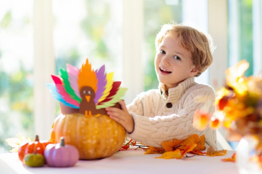 A boy holding a crafted paper turkey over a pumpkin.