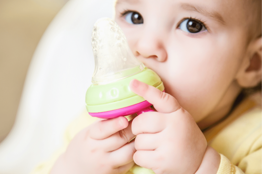 6 month old baby sitting in high chair with a nibbler.