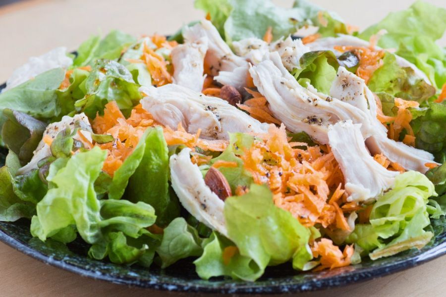 A plate with chicken, carrot and lettuce salad.