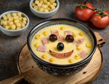 A bowl of ham and corn chowder with a silly face drawn on top.